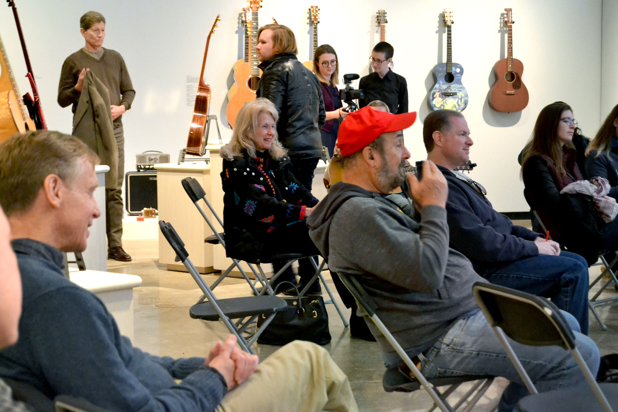 Image of an audience watching a bluegrass performance with a background of hanging guitars