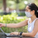 Woman sitting outside wearing a mask next to a laptop